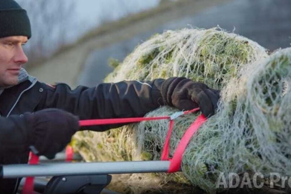 ADAC-Sicherheitsingenieur Maximilian Bauer demonstriert, wie ein Christbaum richtig auf dem Dachträger befestigt wird.