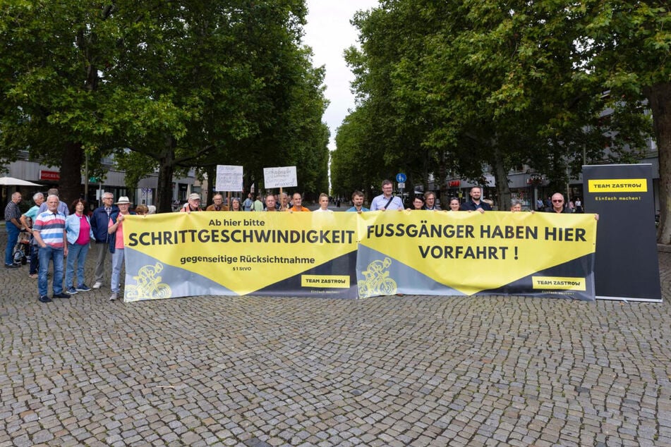 "Ab hier bitte Schrittgeschwindigkeit", "Fußgänger haben hier Vorfahrt": Mit einer Banner- und Plakataktion will Team Zastrow (TZ) mit Unterstützern die Hauptstraße wieder sicherer für Fußgänger machen.