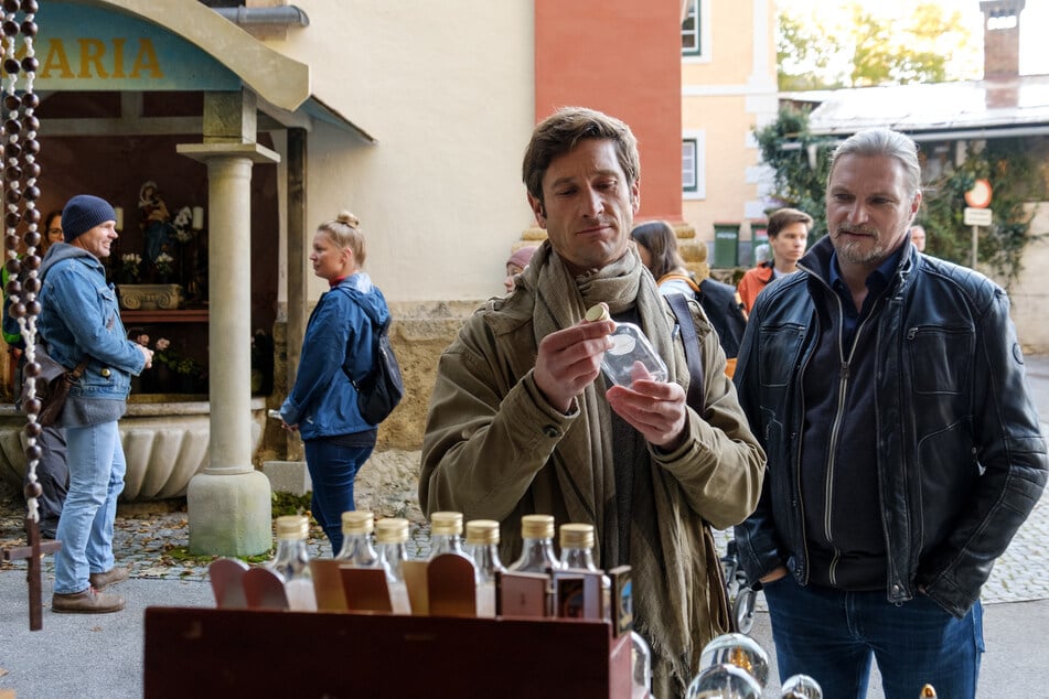 Bezirksinspektor Klaus Lechner (Andreas Kiendl) findet einen Stand in Mariazell, wo heiliges Wasser verkauft wird. Major Carl Ribarski (Stefan Jürgens) steht neben ihm und beobachtet, wie sein Kollege ein Fläschchen betrachtet.