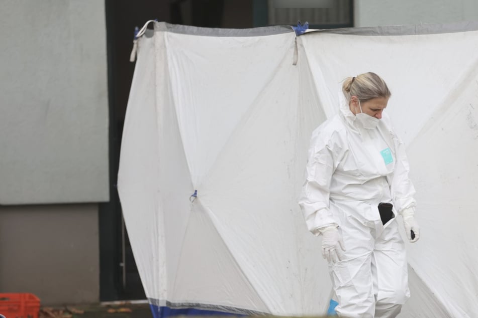 Eine Mitarbeiterin der Spurensicherung untersucht den Tatort vor dem Wohnblock in der Ackerstraße in Köln-Mülheim.