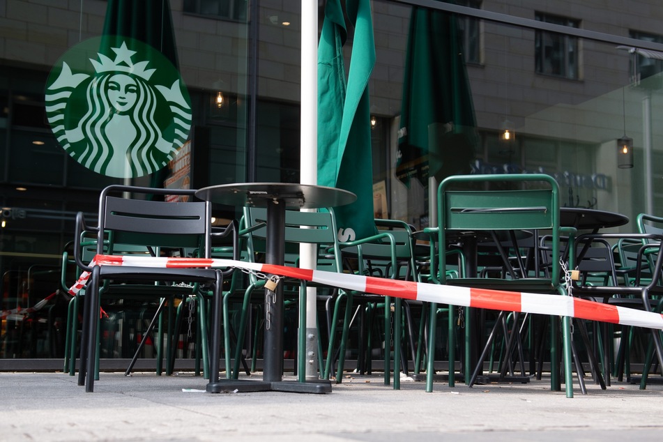Symbolisch: Ein Absperrband umgibt Stühle und Tische einer Starbucks-Filiale.