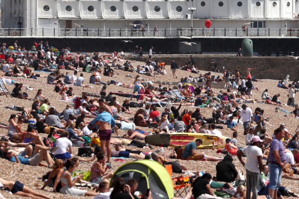 Die Menschen genießen das Wetter am Strand am Brighton Palace Pier.