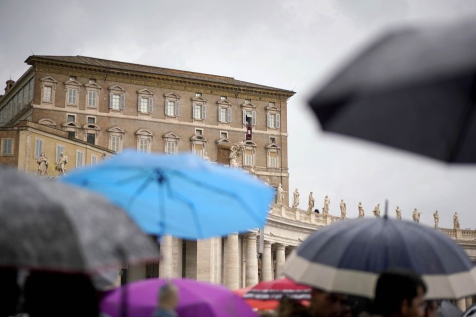 Menschen stehen unter Regenschirmen auf dem Petersplatz, um den Segen von Papst Franziskus zu empfangen.