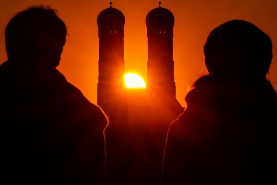 Ein Pärchen schaut der Sonne zu, die hinter der Frauenkirche mit ihren beiden 99 Meter hohen Türmen im Herzen der bayerischen Landeshauptstadt untergeht.