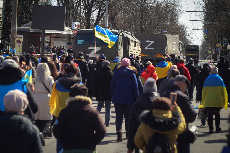 Menschen mit ukrainischen Fahnen gehen während einer Kundgebung gegen die russische Besatzung in Cherson am 20. März 2022 auf Lastwagen der russischen Streitkräfte zu.