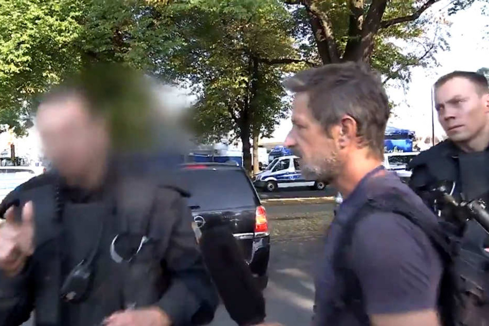 Darum geht es: Polizisten stellen die Personalien von TV-Reporter Arndt Ginzel (r.) fest. Vorher war ein Kameramann Ginzels von einem Demonstranten zur Polizei gedrängt worden.