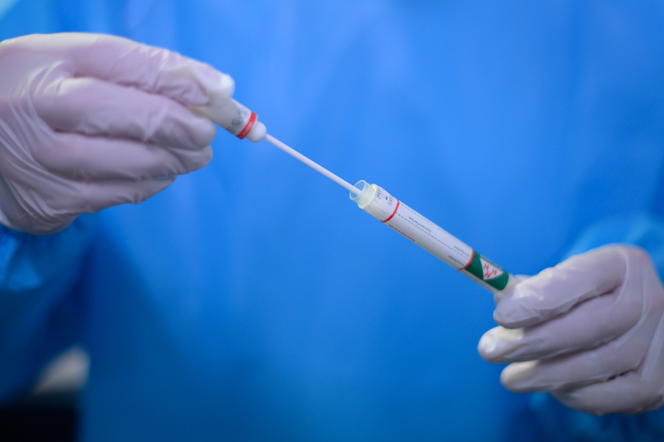 Ein Arzt der Kassenärztlichen Vereinigung Sachsen hält in der Corona-Teststation für Urlaubsrückkehrer am Flughafen Dresden International einen Coronavirus-Test in den Händen.