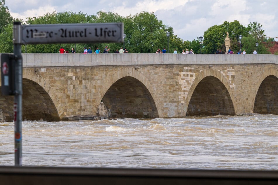 Menschen stehen in der Regensburger Altstadt auf der Steinernen Brücke und schauen sich das Hochwasser an.