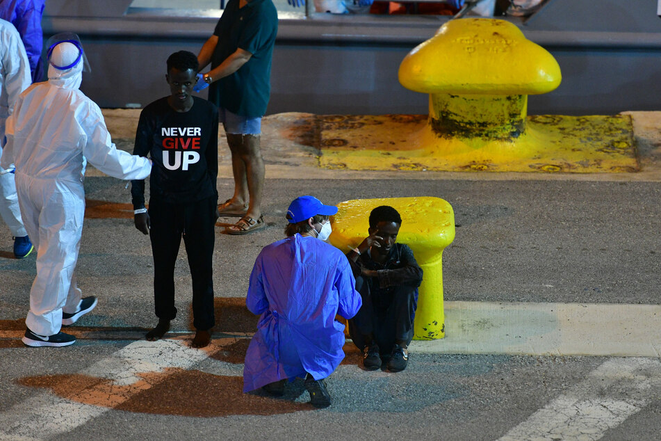 Helfer sprechen im Hafen von Malta mit zwei Migranten am Boiler Wharf.