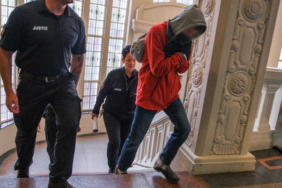 Der Angeklagte betritt in Begleitung von zwei Justiz-Beamten das Gericht.