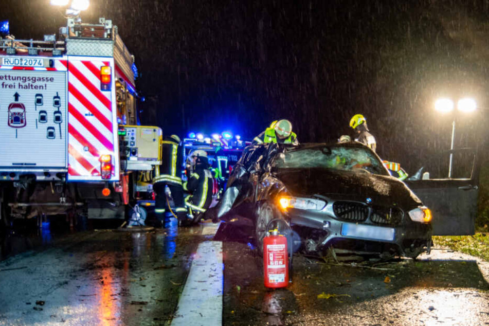 Einsatzkräfte stehen um das zerquetschte Fahrzeug herum.