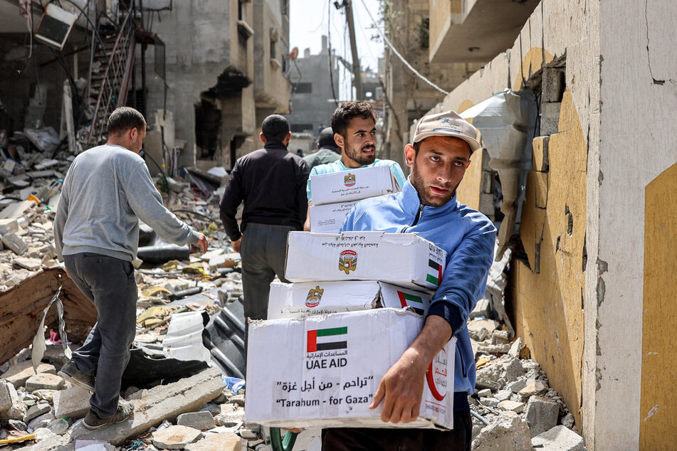 Men walk through rubble past damaged buildings with humanitarian aid packages collected from a drop over the northern Gaza Strip on Tuesday amid the ongoing conflict in the Palestinian territory between Israel and the militant group Hamas.