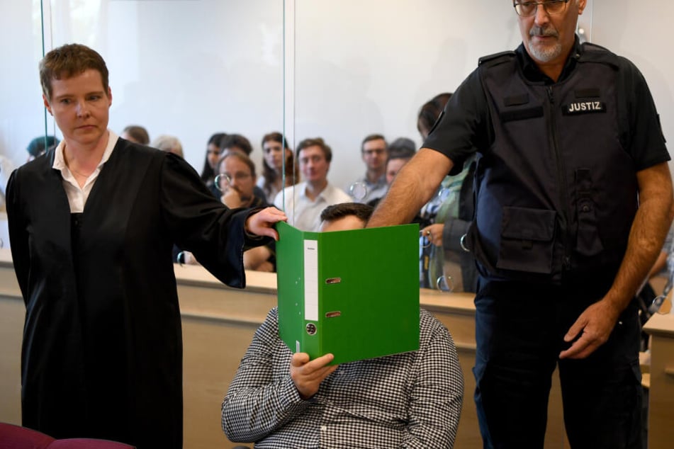 Mit verdecktem Gesicht sitzt der Angeklagte zum Auftakt eines Mordprozesses im Gerichtssaal.