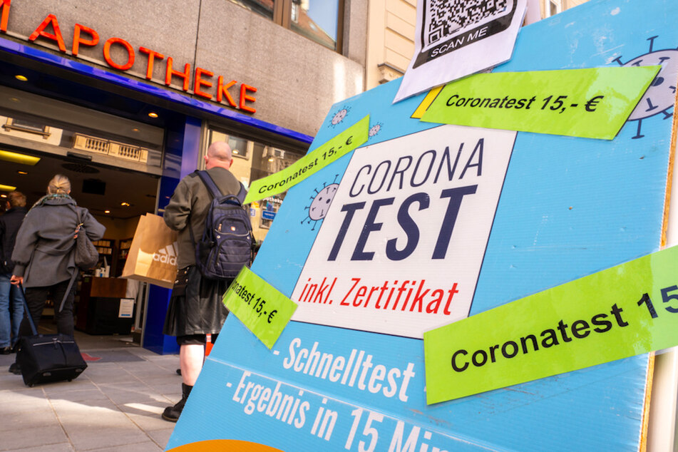 Passanten stehen in der Münchner Innenstadt vor einer Apotheke, die Coronatests für 15 Euro anbietet.
