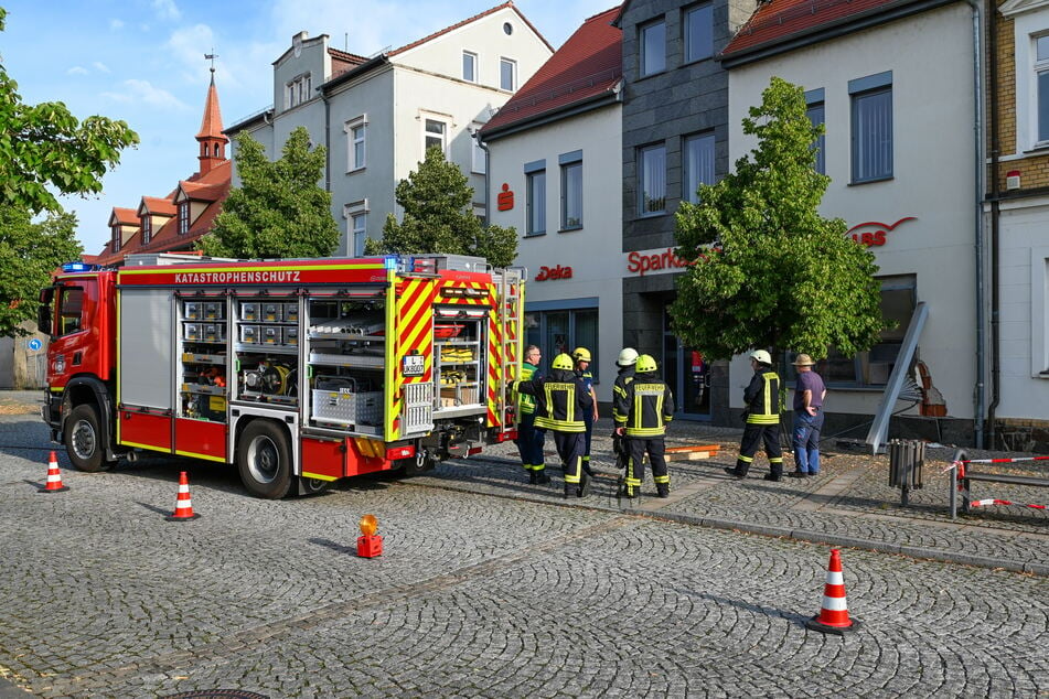 Auf dem Markt in Brandis betrachten Feuerwehrleute und THW-Helfer die Schäden am direkt neben dem Rathaus gelegenen Sparkassen-Gebäude.