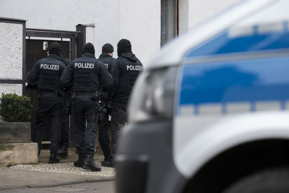 Polizisten und ein Polizeiwagen stehen vor einem Wohnhaus. (Symbolbild)