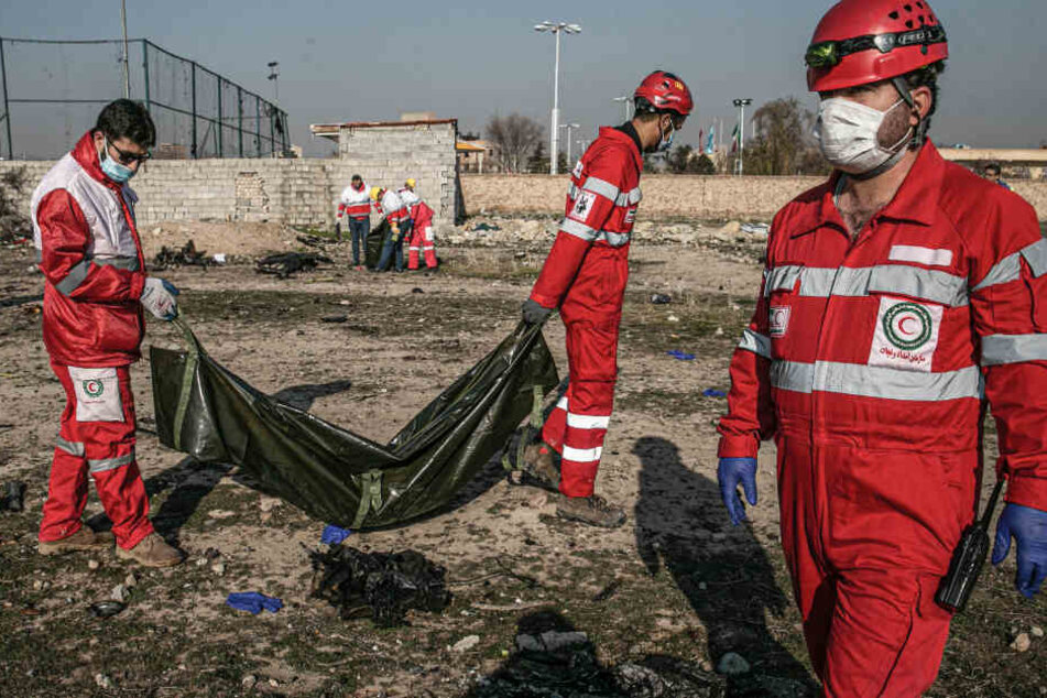 Rettungskräfte tragen die sterblichen Überreste eines Absturzopfers in einem Leichensack.