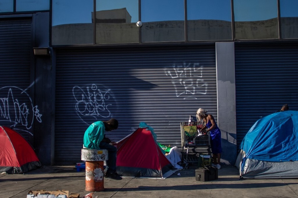 Unhoused people stand next to an encampment in Skid Row, downtown Los Angeles, California.