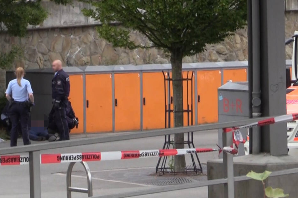 Polizisten stehen am Stadtbahnhof neben dem festgenommenen Tatverdächtigen, der am Boden liegt.