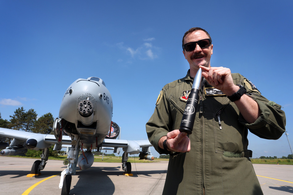 Brad Lynch, Pilot der US-Airforce, hält bei einem Medientag zur "Air Defender 2023" vor einem Kampfflugzeug A10 der Airforce eine 30mm Patrone mit denen dieser Flugzeugtyp bestückt ist.