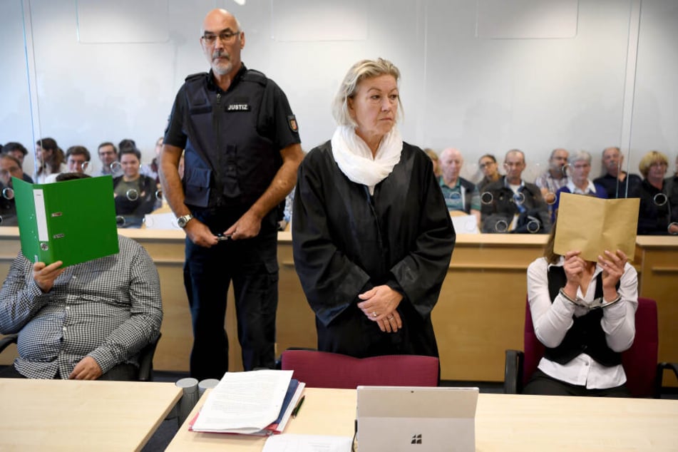 Mit verdeckten Gesichtern sitzen die Angeklagten neben ihrer Anwältin im Gerichtssaal.