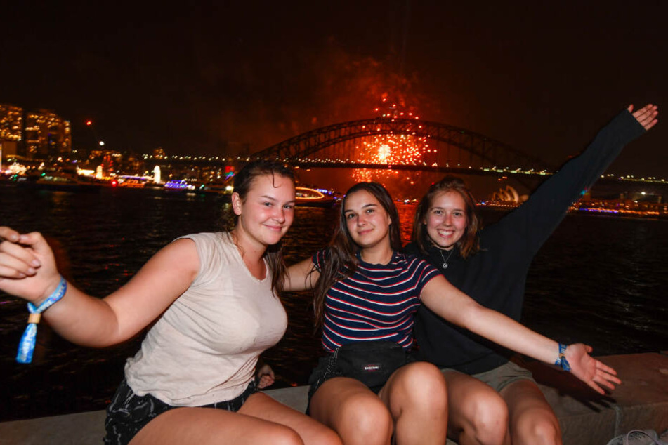 Die Touristinnen Paula Nobbe (l-r), Alina Wegmann und Finja Kirchhoff aus Deutschland sitzen für ein Foto während des Familien-Feuerwerks "The 9pm Family Fireworks" im Hafen zusammen.