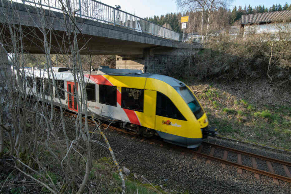 Ein Zug der Hessischen Landesbahn fährt unter einer Brücke durch. Mehrere Gullydeckel waren auf Höhe der Fahrerkabine an Seilen von der Brücke festgebunden.