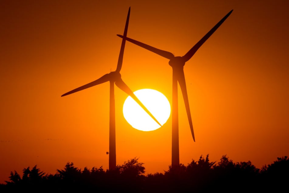 Die Sonne geht hinter zwei Windrädern unter.