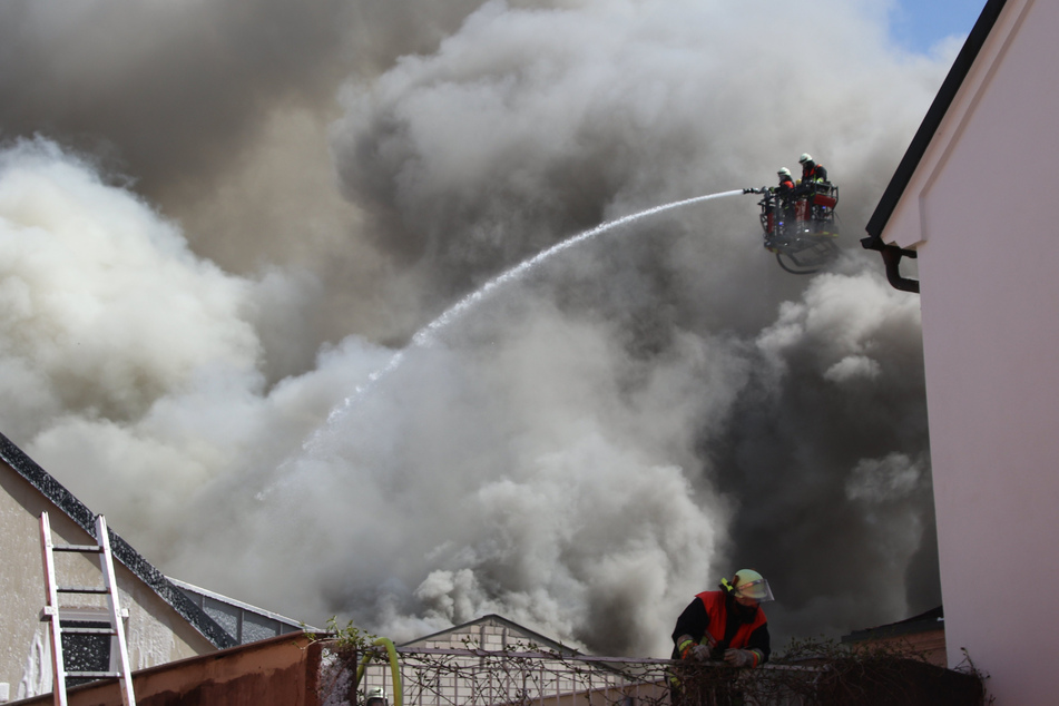 Einsatzkräfte der Feuerwehr versuchen den Brand im Dachstuhl einer Lagerhalle zu löschen, der teilweise auf anliegende Gebäude übergriff.