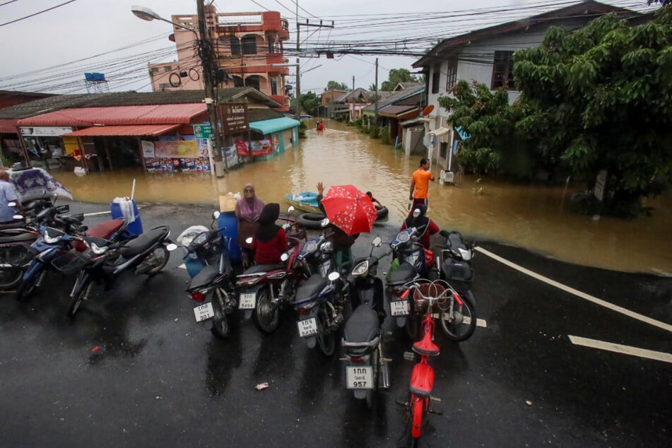 People stand next to their motorcycles on a road and look at the floods in the southern province of Pattani.