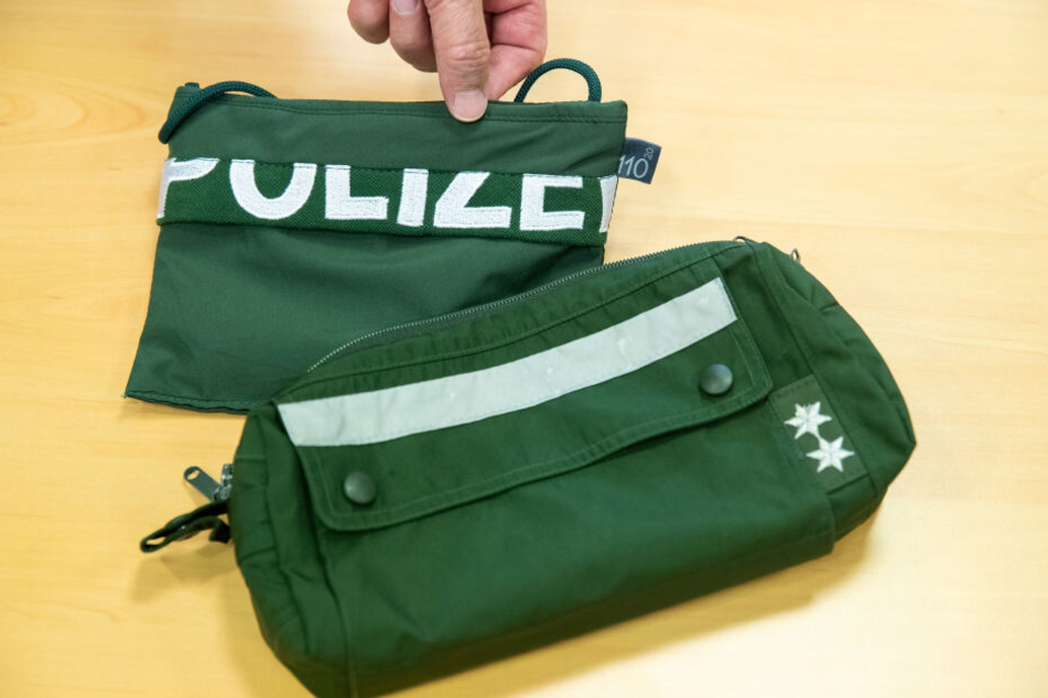 Ein Brustbeutel und eine Fahrrad-Lenkertasche gefertigt aus Stoffen alter Polizei-Uniformen liegen auf einem Tisch.