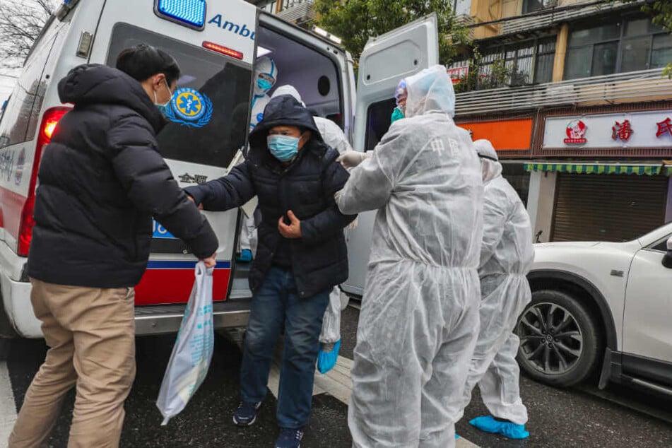 Krankenhausmitarbeiter in Schutzkleidung helfen einem Patienten in Wuhan aus einem Krankenwagen.