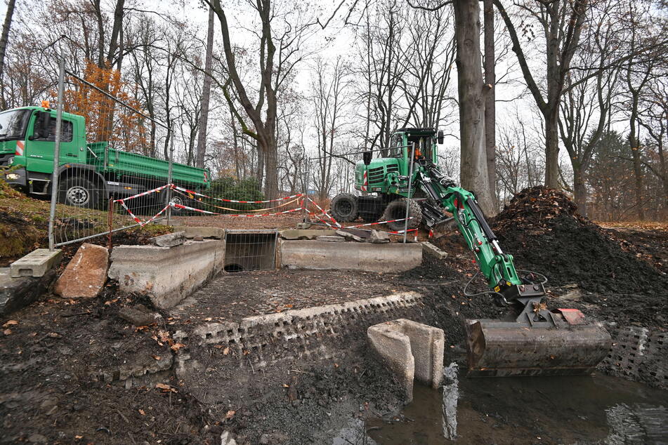 Mitarbeiter des Grünflächenamtes baggern Schlamm aus und setzen den Teichablauf instand.