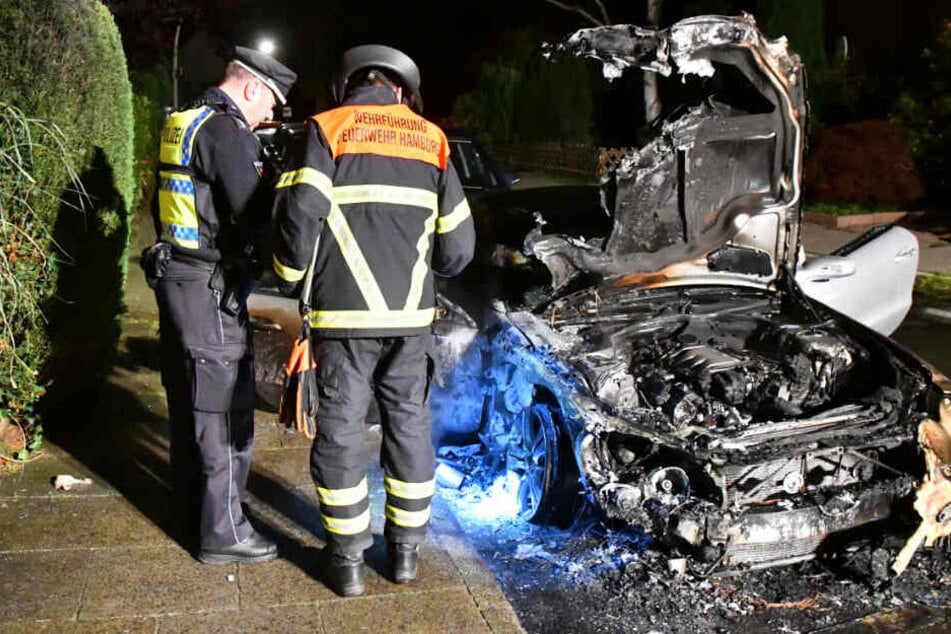 Polizei und Feuerwehr untersuchen ein ausgebranntes Auto.
