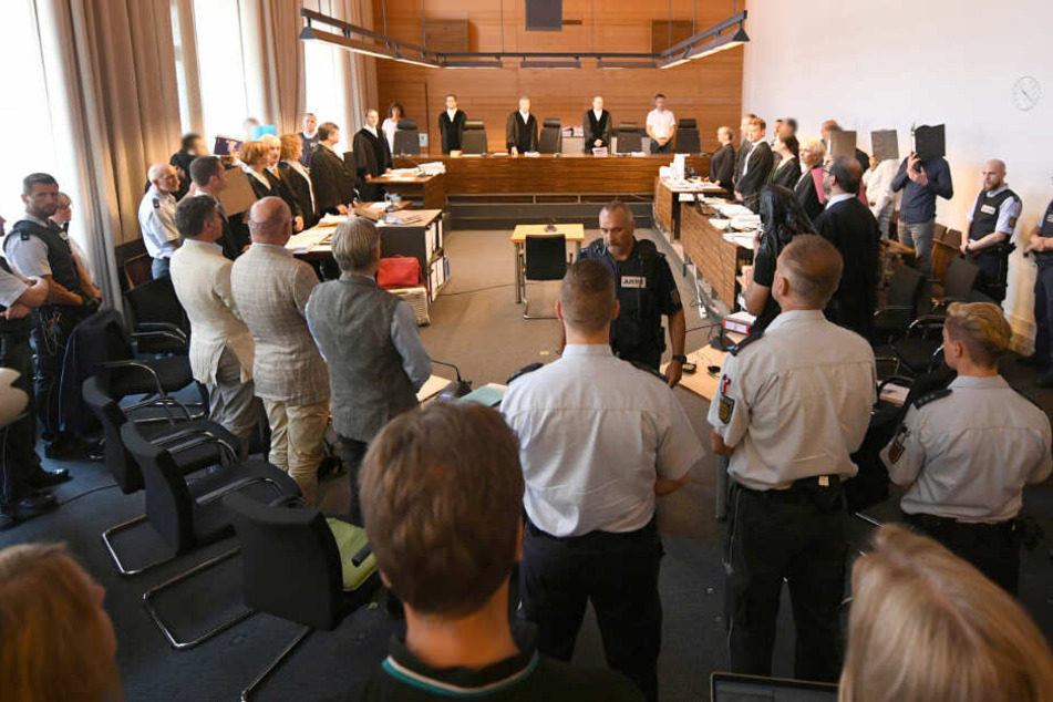 Zu Beginn des Prozesses stehen elf Angeklagte und Justizbeamte im Landgericht seitlich hinter ihren Anwälten. (Archivbild)