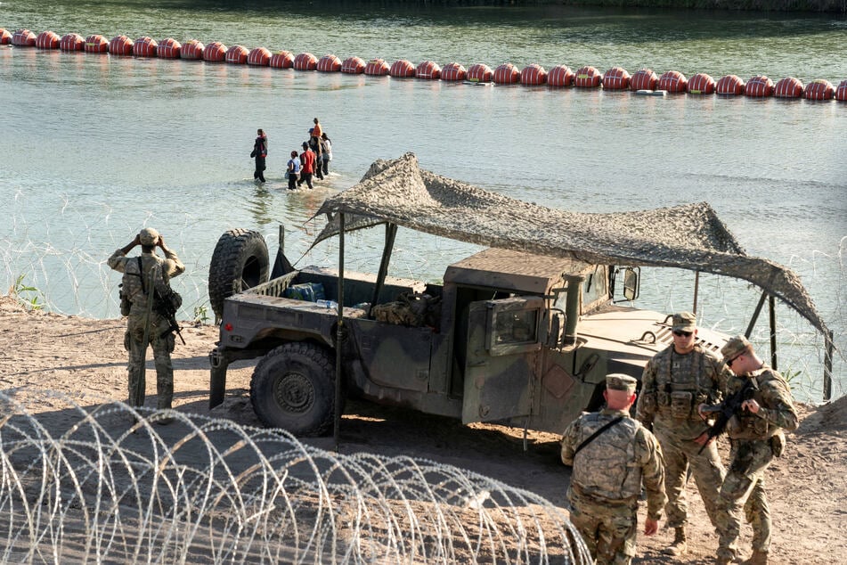 Asylum-seeking migrants walk in the Rio Grande river between the floating barricade and the river bank as they look for an opening on a concertina wire fence to land in Eagle Pass, Texas.