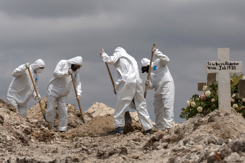 Mexiko, Tijuana: Arbeiter in Schutzanzüge schaufeln Erde bei einer Beerdigung im Rahmen der Covid-19-Pandemie. Im staatlichen Friedhof Nr. 13 werden Covid-19-Todesopfer unter Einhaltung besonderer Maßnahmen bestattet.