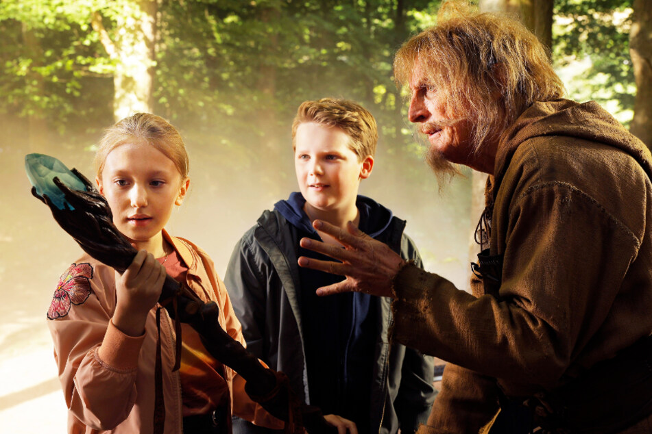 Catweazle (Otto Waalkes, r.) zeigt Lisa (l., Gloria Terzic) und Benny (Julius Weckauf), wie man mit einem Zauberstab richtig umgeht.