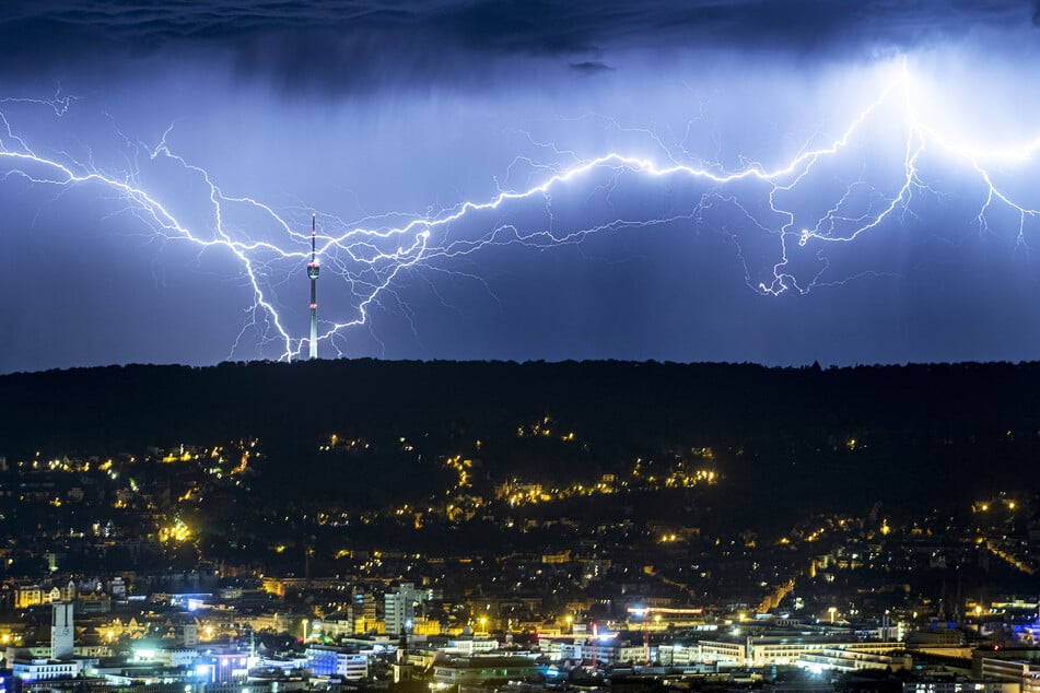 Blitze zucken des Nachts hinter dem beleuchteten Stuttgart am Horizont, und schlagen nahe des Fernsehturms ein.