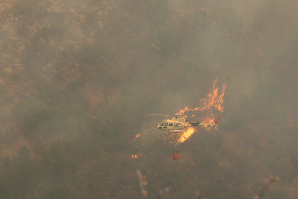 Ein Hubschrauber fliegt über einen Waldbrand, der sich ausgebreitet hat.