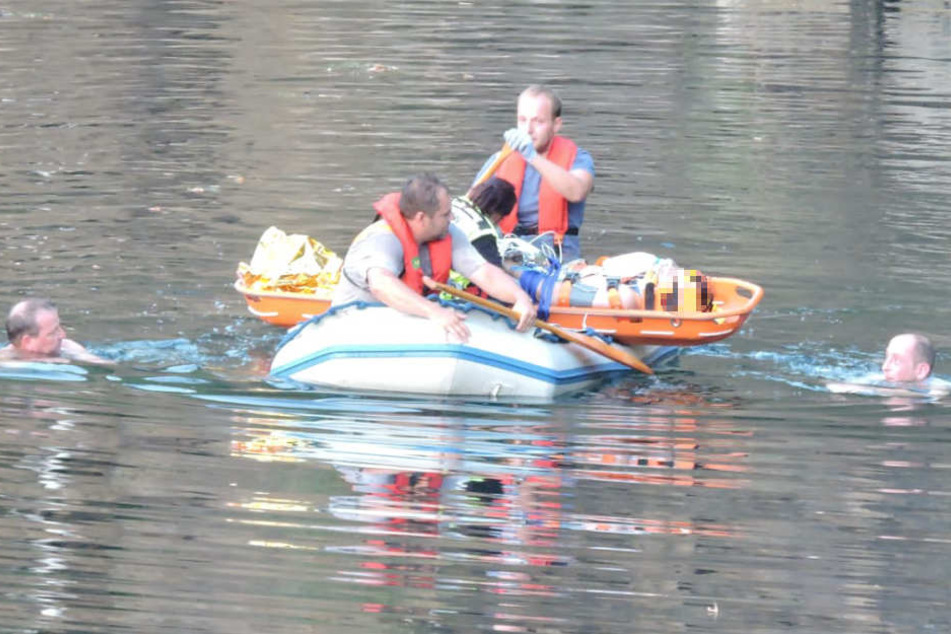 Rettungskräfte bringen den Mann zum Abtransport an eine geeignetere Stelle. Zur Absicherung schwimmen zwei Feuerwehrmänner neben dem Boot her.