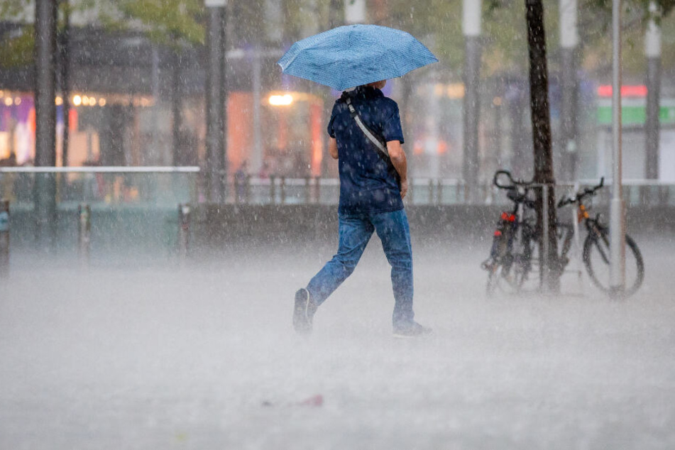 Ein Fußgänger spaziert mit einem Regenschirm durch den Regen.