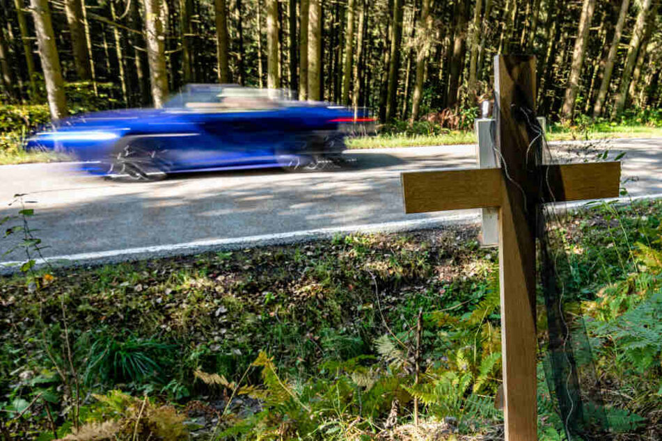 Ein Holzkreuz steht an der Unfallstelle, an der zwei Männer ein verbotenes Rennen mit einem Auto beziehungsweise Motorrad veranstaltet und dabei den Tod eines weiteren Autofahrers verursacht haben sollen.