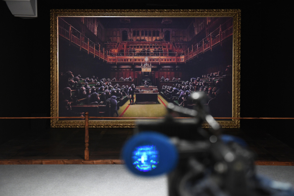 Eine Kamera filmt in der Ausstellung "The Mystery of Banksy – A Genius Mind" bei einem Presserundgang eine Reproduktion einer Arbeit des Künstlers Banksy mit dem Titel "Devolved Parliament."