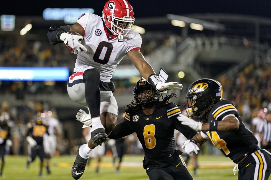 Darnell Washington (l) of the Georgia Bulldogs leaps while running the ball against the Missouri Tigers.