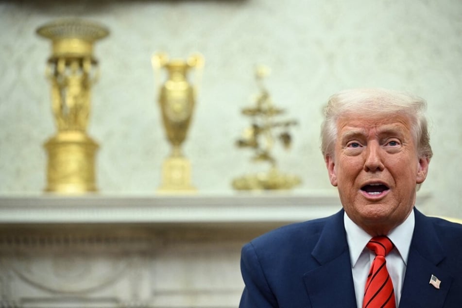 President Donald Trump sits surrounded by gold trophies in the Oval Office of the White House.