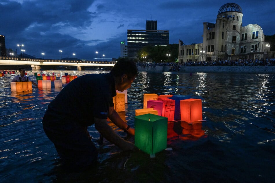 Volunteers (L) push paper lanterns out onto the Motoyasu River past the Atomic Bomb Dome (back R) after they were released by visitors to mark the 80th anniversary of the world's first atomic bomb attack, in the city of Hiroshima on Wednesday.
