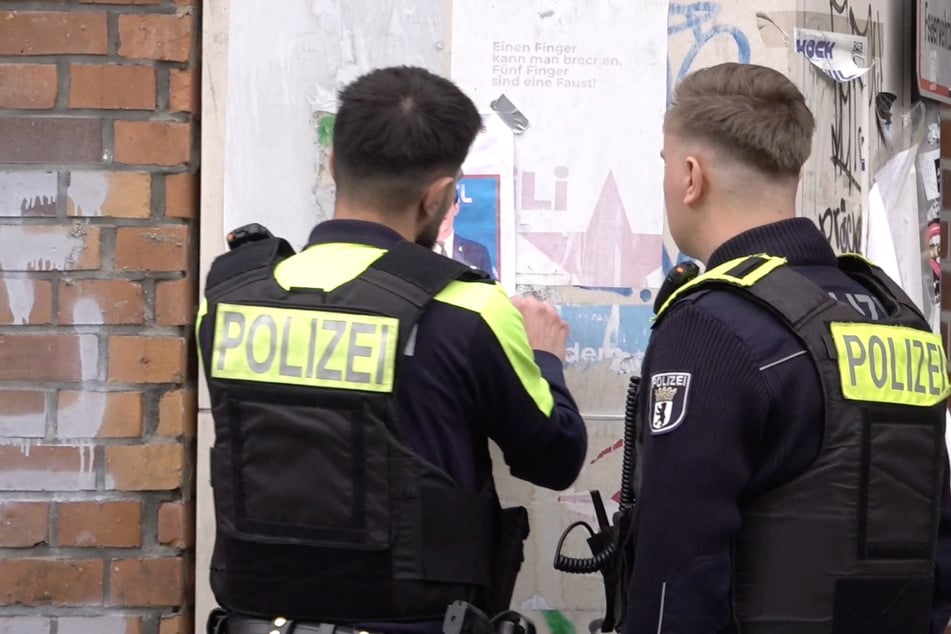 In Berlin-Mitte entfernen Polizisten am Freitag ein Plakat, das den erschossenen Deutsch-Israeli Yaron Lischinsky (†30) unter einem roten Dreieck zeigt.