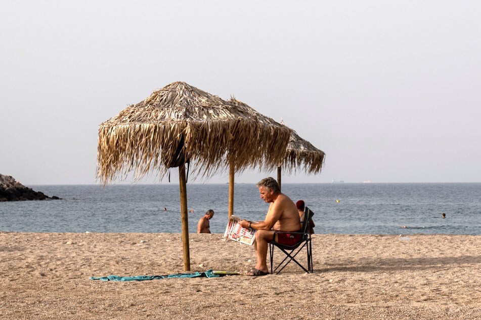 Schwitzen im warmen Griechenland: Ein Mann liest eine Zeitung an einem Strand in Glyfada (Athen).