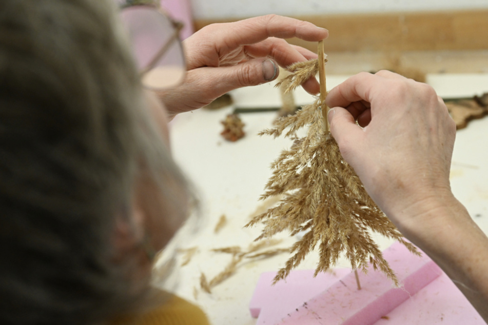 Aus getrockneten Gräsern fertigt eine Kursteilnehmerin einen Baum für eine Krippe.